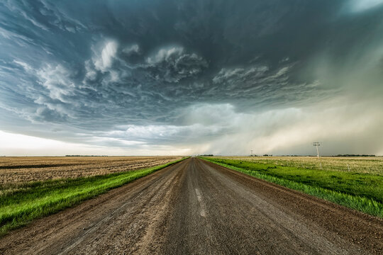 Gravel road leading into the distance towards dramatic storm clouds; Val Marie, Saskatchewan, Canada