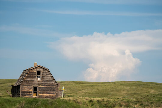 Abandoned barn on farmland with unique cloud formation in the distance; Val Marie, Saskatchewan, Canada