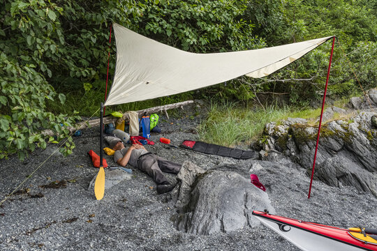 Kayaker resting under a tarp on a beach in Prince William Sound; Alaska, United States of America