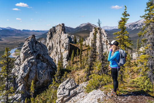 Woman talking on cell phone on top of Sapper Hill while hiking along the Dempster Highway enjoying the scenery on a sunny day; Yukon, Canada