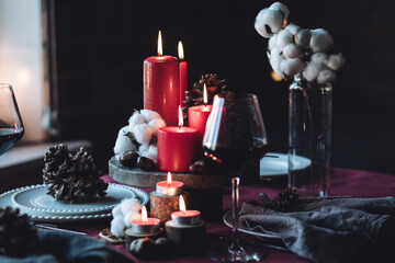 Rustic table decor for Christmas or New Year family dinner. Centrepiece with red candle, dry orange, cone, cinnamon, anise. Zero waste eco-friendly home. Cozy atmosphere, dark background. Close up