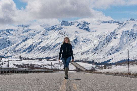 Woman walking along the Haines Highway during a late May, sunny day; Yukon, Canada