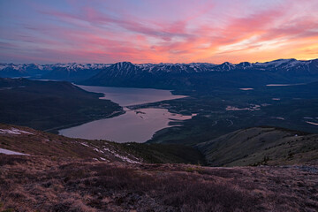 Midnight sun illuminates the sky in a blaze of colour during summer solstice above Bennett Lake and Carcross, Yukon; Carcross, Yukon, Canada