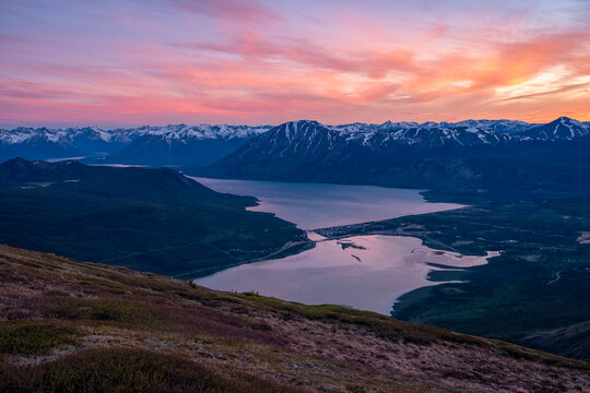 Midnight sun illuminates the sky in a blaze of colour during summer solstice above Bennett Lake and Carcross, Yukon; Carcross, Yukon, Canada