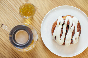 Close up shot of delicious Cinnabon on table with cup of tea and teapot.