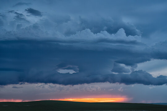 Storm clouds gather over silhouetted landscape at dusk; North Dakota, United States of America