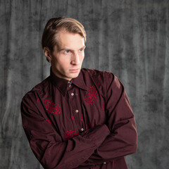 an attractive man in an elegant suit, burgundy shirt with embroidery. Photo in the studio on a gray background