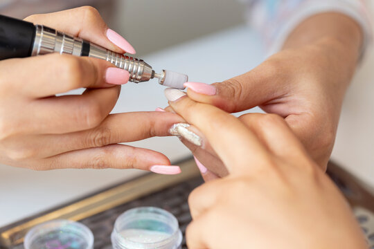 Closeup of manicurist sanding the acrylic nails of a customer. A nail technician performs a manicure in a spa or salon. Cosmetic beauty gel nails maintenance treatment, soft natural light.
