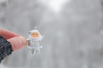 Hand holds santa claus on the background of the winter forest.