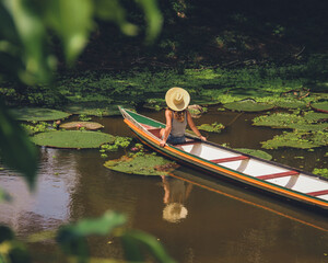 Mulher não identificada, de costas, com chapéu, em barco no rio croa, cercado de...