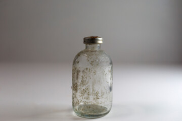 One dirty clear glass medical vaccine bottle, aged and patina on a white background.