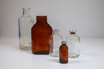 One glass test tube, one amber glass medical pill bottle, two clear glass vaccine bottles, and one small amber vaccine bottle on a white back ground.