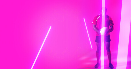 Full length of african american rugby player holding ball over illuminated lines on pink background