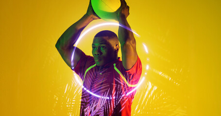 African american rugby player holding ball looking away by illuminated plants and circle