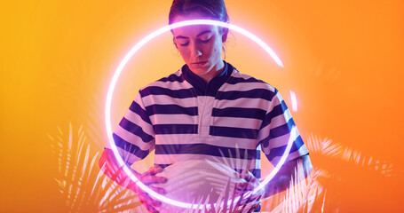 Female caucasian player with ball standing over illuminated circle and plants on orange background