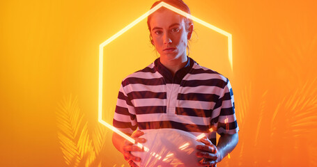 Female caucasian player with ball standing over illuminated hexagon and plants on orange background