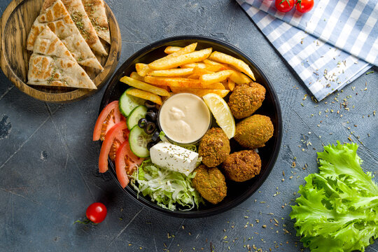 falafel balls in the dish with french fries and vegetables on grey concrete table top view