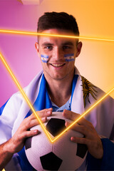 Portrait of caucasian male player with soccer ball and flag of argentina by illuminated triangle