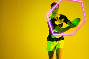 Caucasian male rugby player catching ball by illuminated hexagon over yellow background