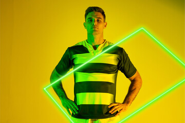 Caucasian rugby player with hands on hip standing by illuminated rectangle over yellow background