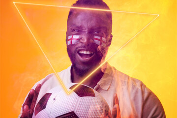 African american male fan with ball and england flag's face paint screaming by illuminated triangle