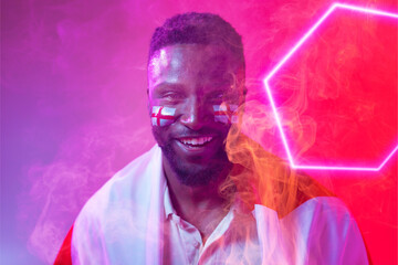African american male fan with england flag and face paint smiling by illuminated hexagon