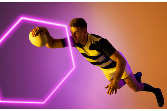 Caucasian male rugby player jumping and catching ball by illuminated hexagon over colored background - Powered by Adobe