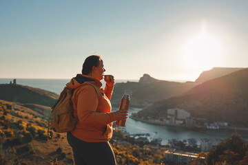 Full girl in an orange jacket, look from the mountain at the sunset.