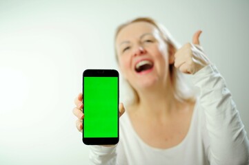 pretty sweet woman in white hoodie looks at the phone, she is glad that she sees there and shows the phone with green screen to camera. Happy lady shares information with us thumbs up show class 