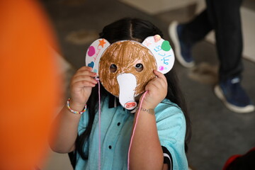 A little child girl wearing a colored animal paper mask fronting her face is isolated in the...