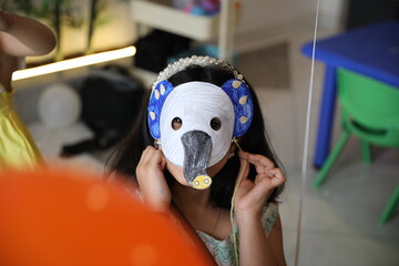 A little child girl wearing a colored animal paper mask fronting her face is isolated in the...