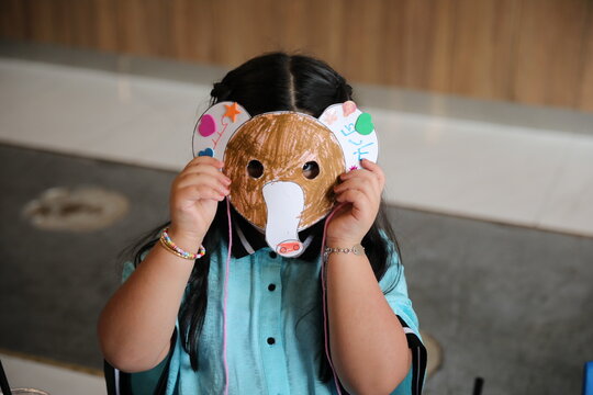 Little child girl wearing a coloured animal paper mask fronting her face, elephant mask crafts.