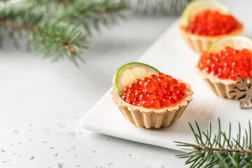 Festive new year appetizer tartlets stuffed with red caviar and a slice of lime on white background with fir branches, text space. Christmas holiday party concept, food recipe