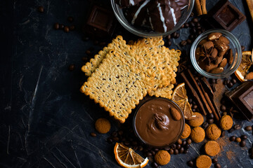 Chocolate paste, nuts, cookies on a dark background