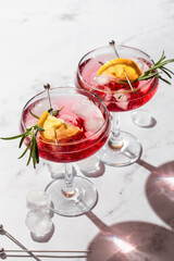 Pomegranate iced cocktail with rosemary and lemon on white marble background isolated with clear shadows in harsh light close up. Xmas or Valentine's drink