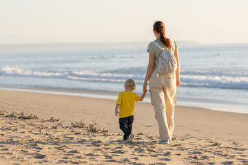 Fototapeta na wymiar Little blonde boy and his mother walking on the beach