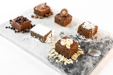 Brownies de chocolate decorados con azúcar, almendras, chocolate, coco, chispas de chocolate y avellana en una mesa de marmol. 