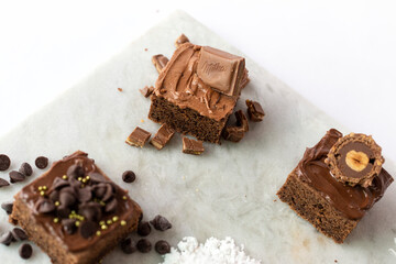 Brownies de chocolate decorados con azúcar, almendras, chocolate, coco, chispas de chocolate y avellana en una mesa de marmol. 