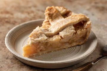 Slice of traditional apple pie on ceramic plate on brown textured background, menu