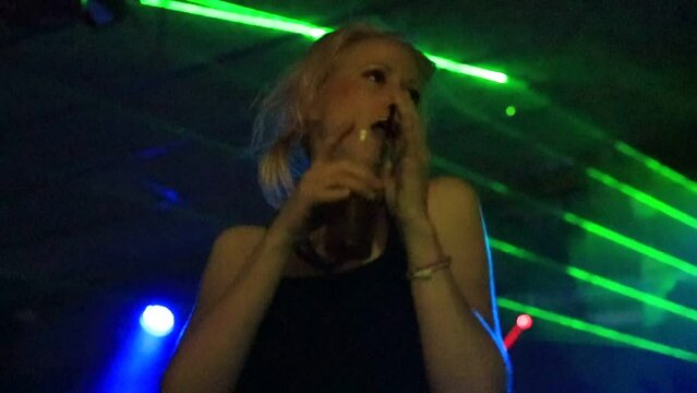 A female dancer with a beverage while performing a sensual dance in a dimly lit nightclub, illuminated by blue-green laser strobe lights. concept of entertainment, relaxation, and nocturnal activities