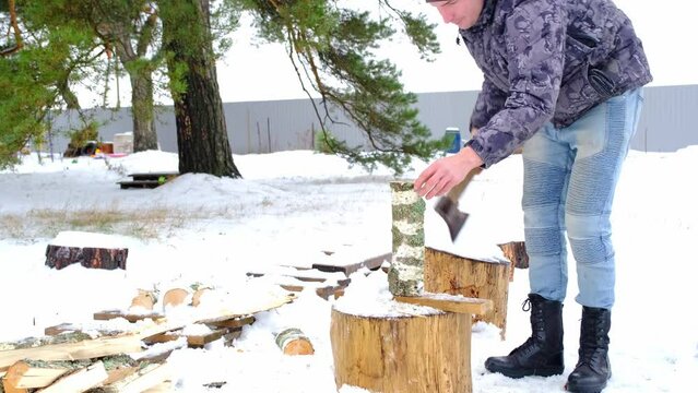 A man is chopping firewood with an axe in winter in the snow. Alternative heating, wood harvesting, energy crisis
