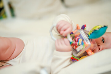 A newborn baby lies on her side and holds an educational toy in her hands. Toy for tactile...