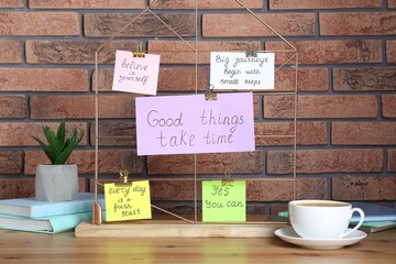 Notes with motivational quotes, coffee, houseplant and books on table against brick wall