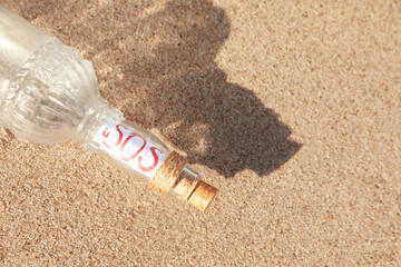 Glass bottle with SOS message on sand, top view