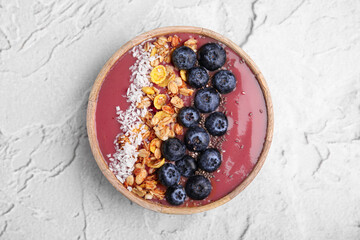 Bowl of delicious fruit smoothie with fresh blueberries, granola and coconut flakes on white textured table, top view