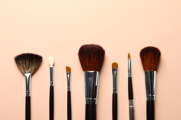 Fototapeta premium Different makeup brushes on light beige background, flat lay . Space for text