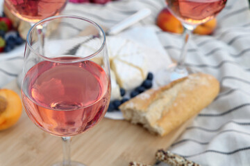 Glasses of delicious rose wine and food on white picnic blanket, closeup