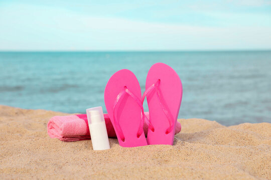 Beach towel, slippers and sunscreen on sand near sea