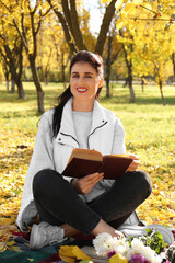 Happy woman reading book in park on autumn day