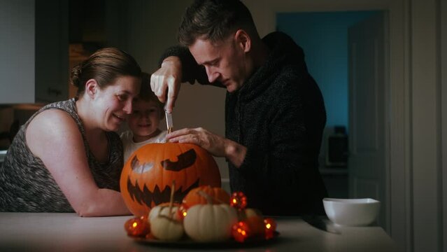 A father carving pumpkin seen by his wife and child. Making jack o lantern.